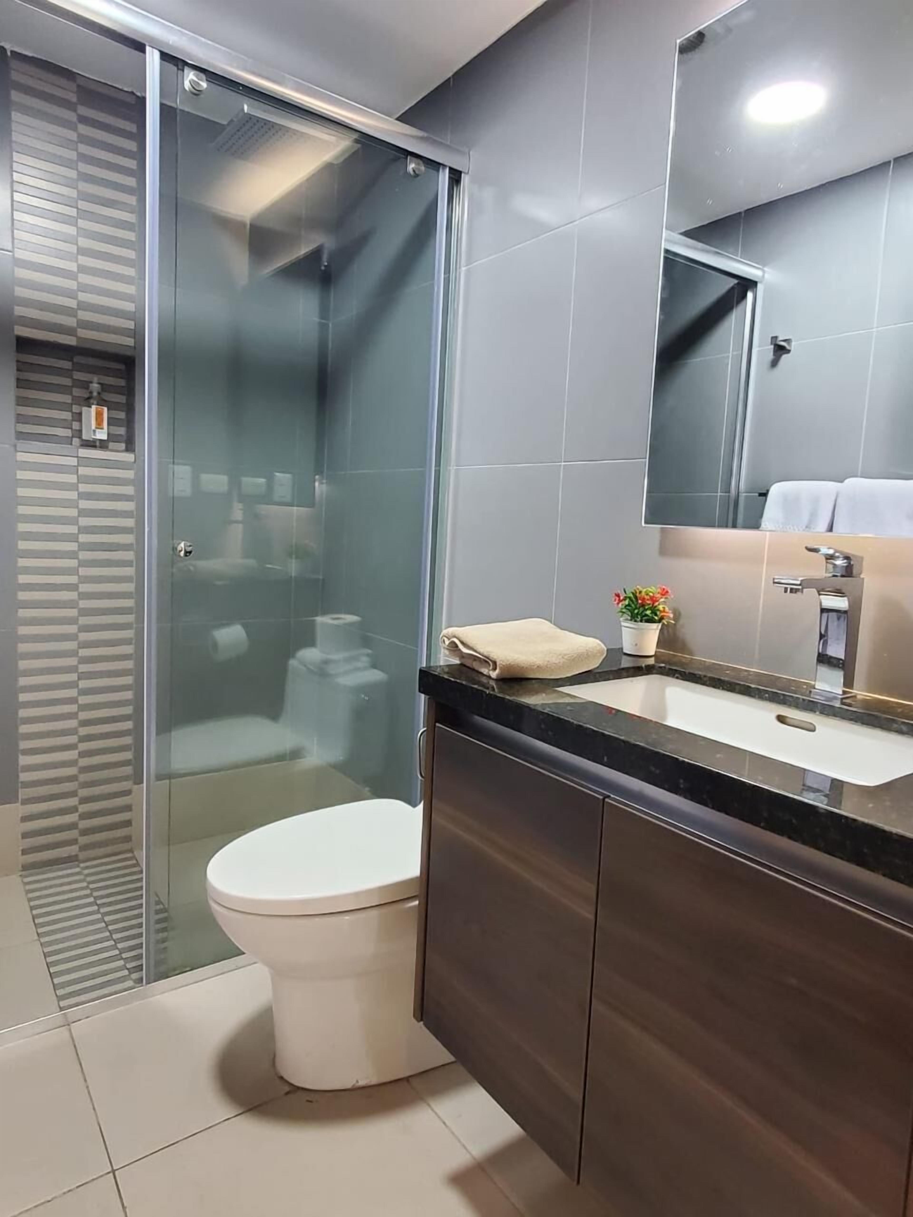 A modern bathroom with a glass shower enclosure, a white toilet, a dark wooden vanity, and a large mirror above the sink.