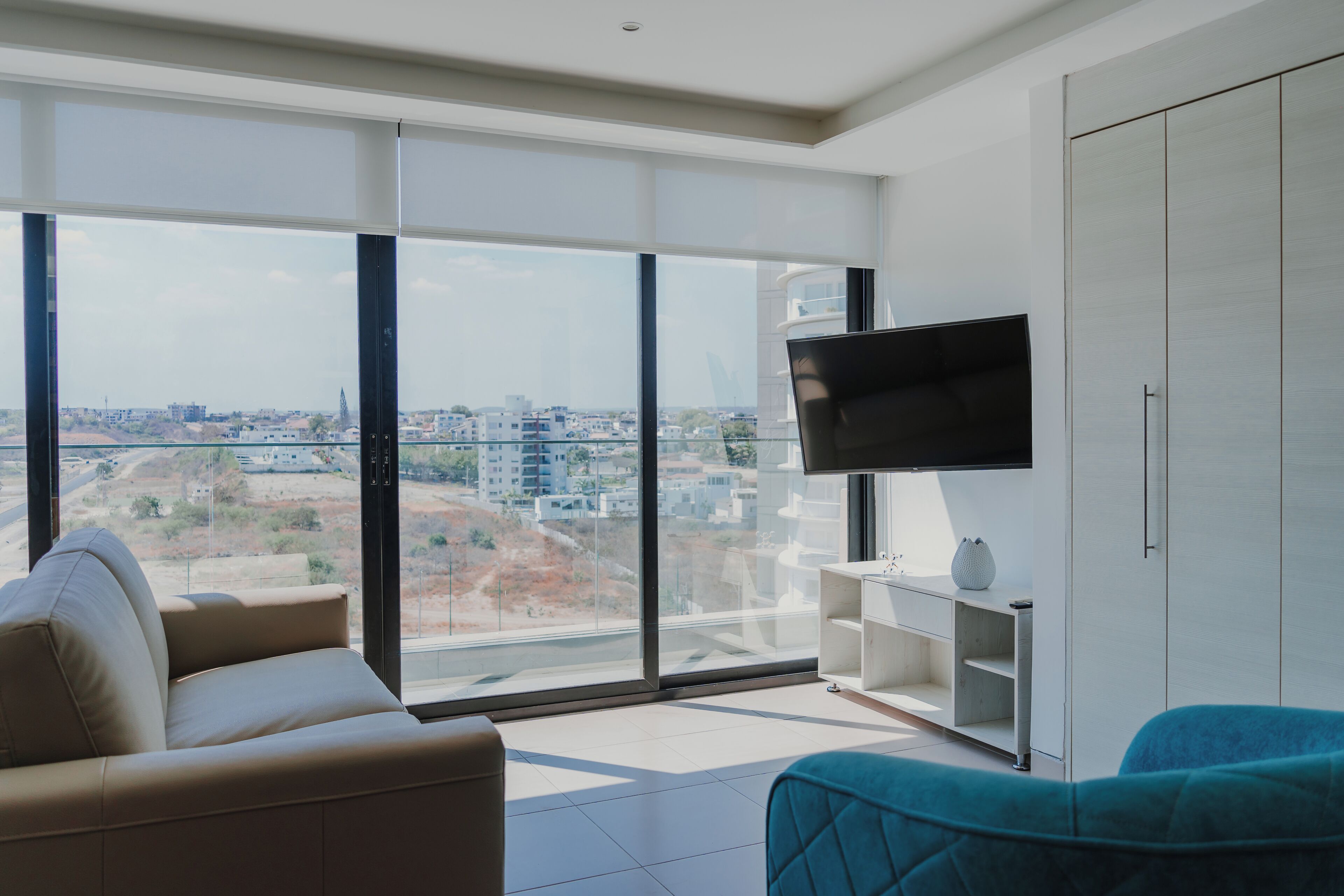 Una sala de estar moderna con un ventanal grande, un televisor de pantalla plana, un sofá y un mueble aparador.