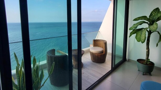 A balcony with a view of the ocean, wicker furniture, and a potted plant.