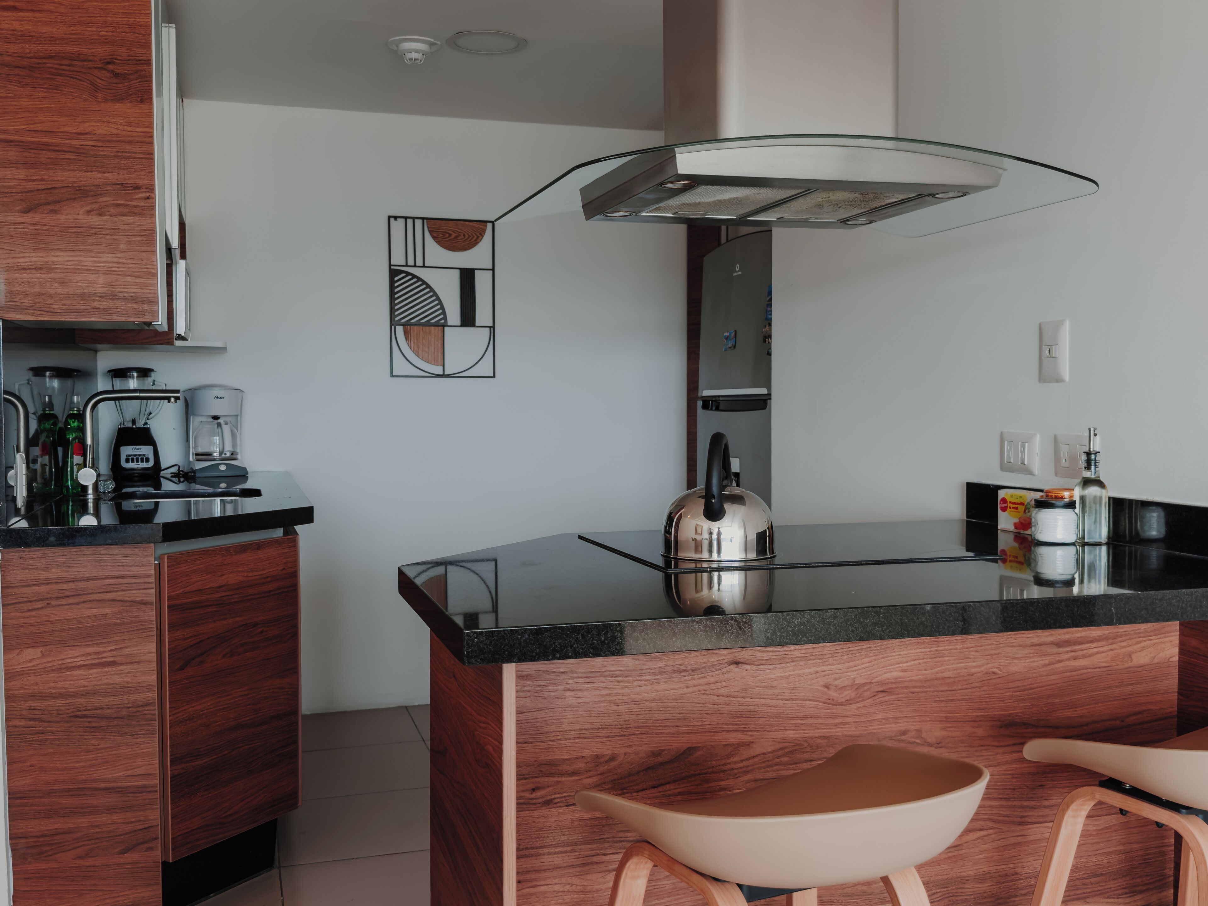 A modern kitchen with a central island, wooden cabinets, a coffee maker, and a kettle.