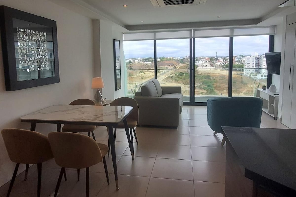 A modern living room with a dining area, large windows, and a view of the cityscape.