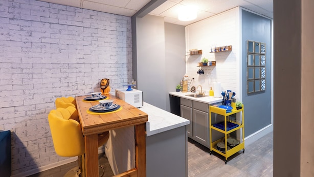 A modern kitchen with a white brick wall, a wooden dining table with yellow chairs, and a small island with a sink.