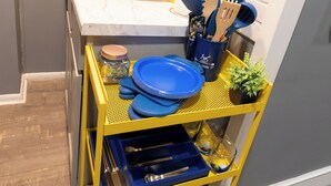 A kitchen with a yellow cart holding blue plates, a sink, and various utensils.