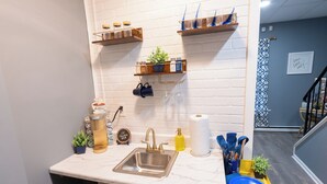 A kitchen with a white brick backsplash, stainless steel sink, and wooden shelves with kitchen items.