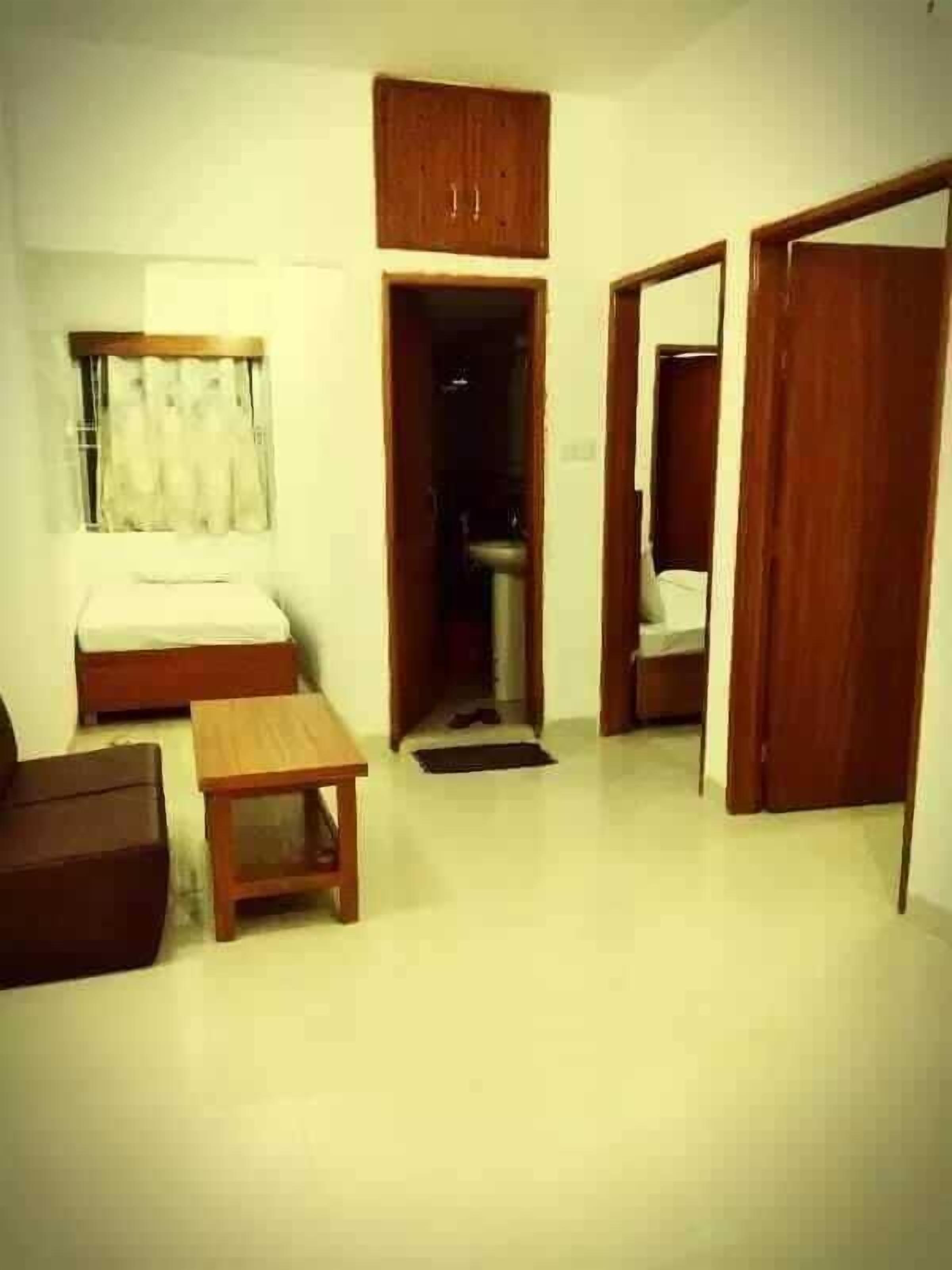 A compact room with a bed, a small table, a wardrobe, and a window with curtains.