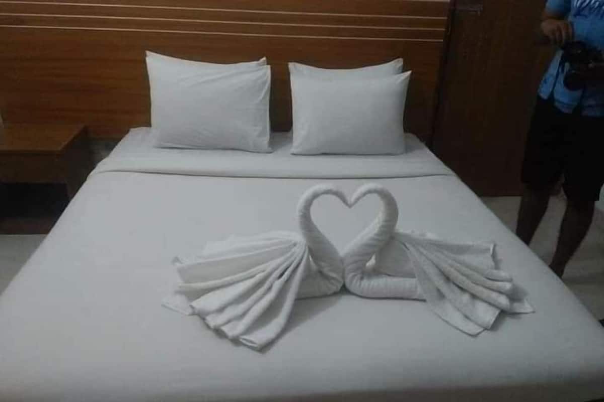 Una cama con sábanas y almohadas blancas, y un arreglo de toallas con forma de corazón sobre la cama, junto con un cabecero de madera.