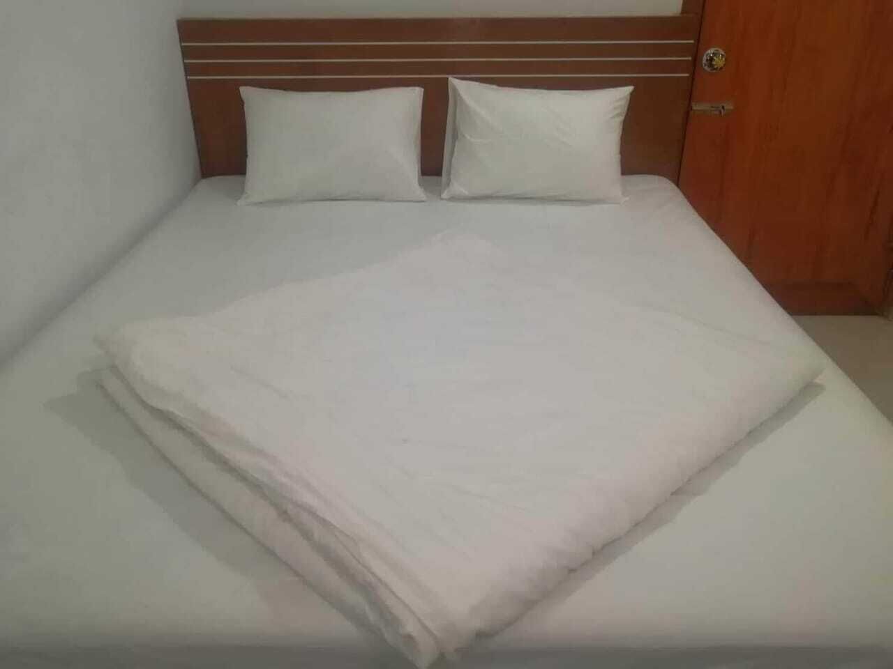 A neatly made bed with white linens and pillows, a wooden headboard, and a wooden door.