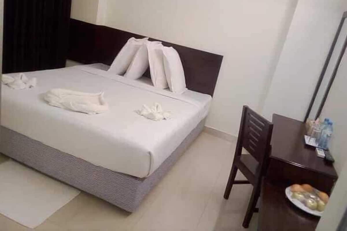 Una cama bien tendida con almohadas y una toalla doblada, una mesita de noche de madera con un plato de comida y una silla.