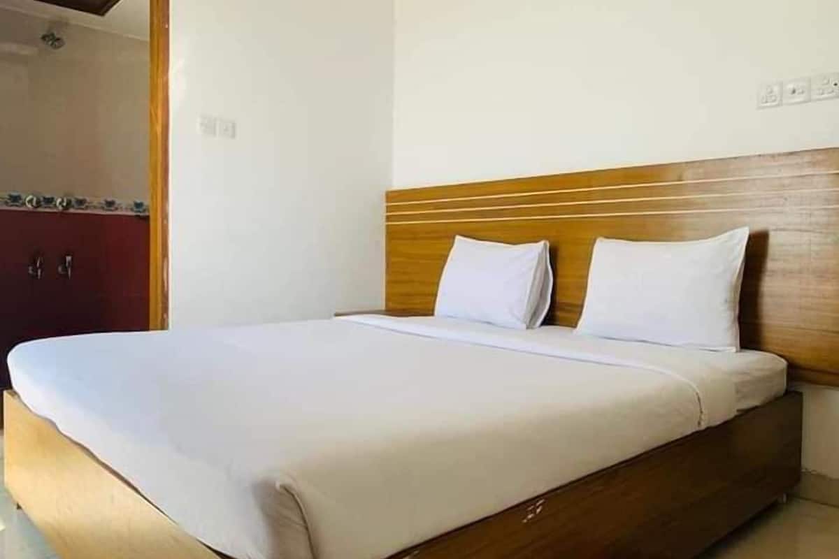 Una cama individual con cabecera de madera y ropa de cama blanca en una habitación con suelo de baldosas.