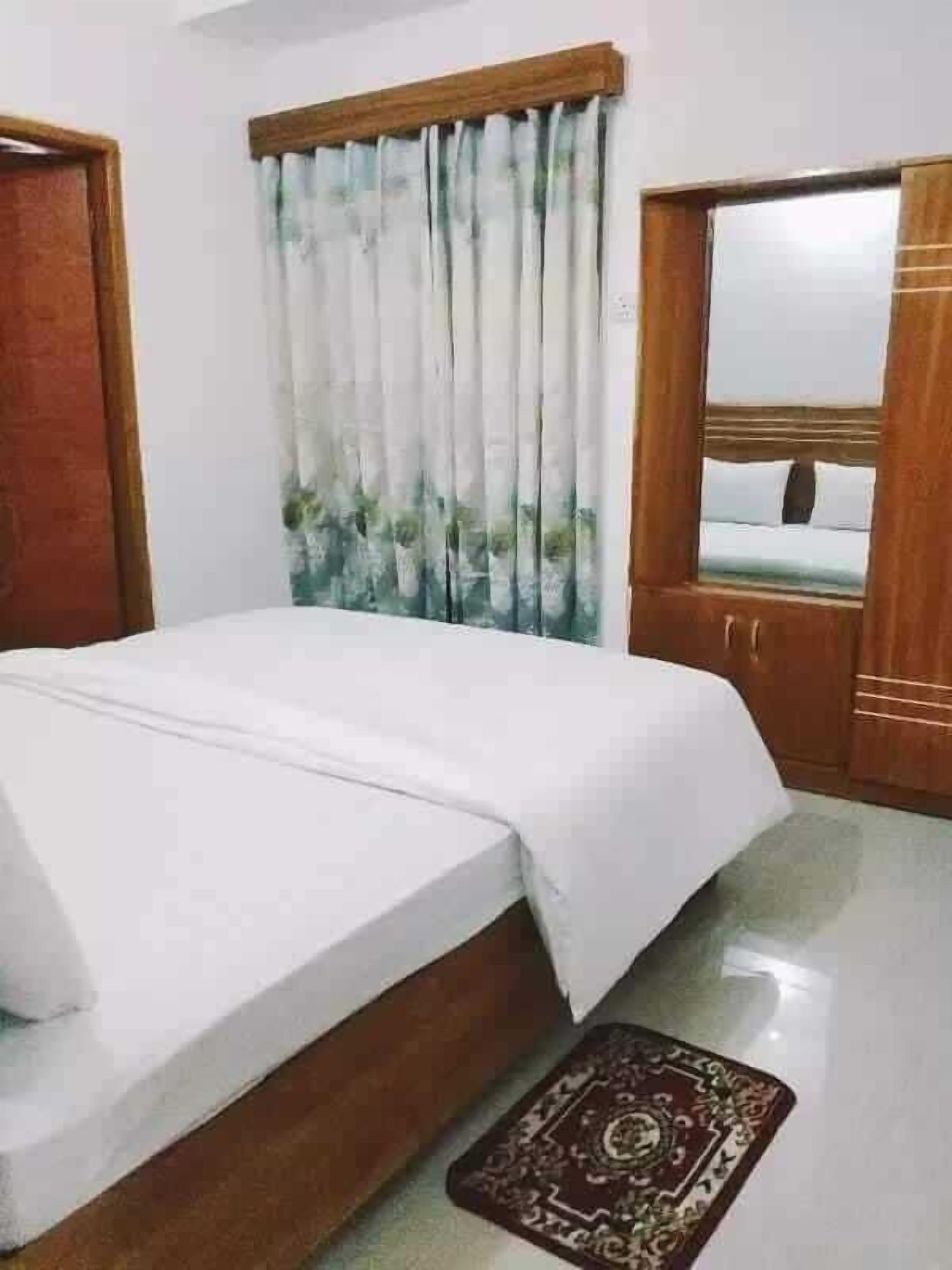 A bedroom with a bed, a wooden wardrobe, a mirror, and a curtain.