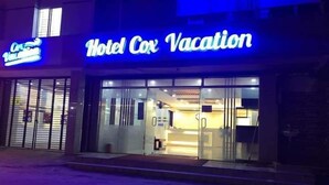 Entrada de un hotel con un letrero de neón que dice "Hotel Cox Vacation".