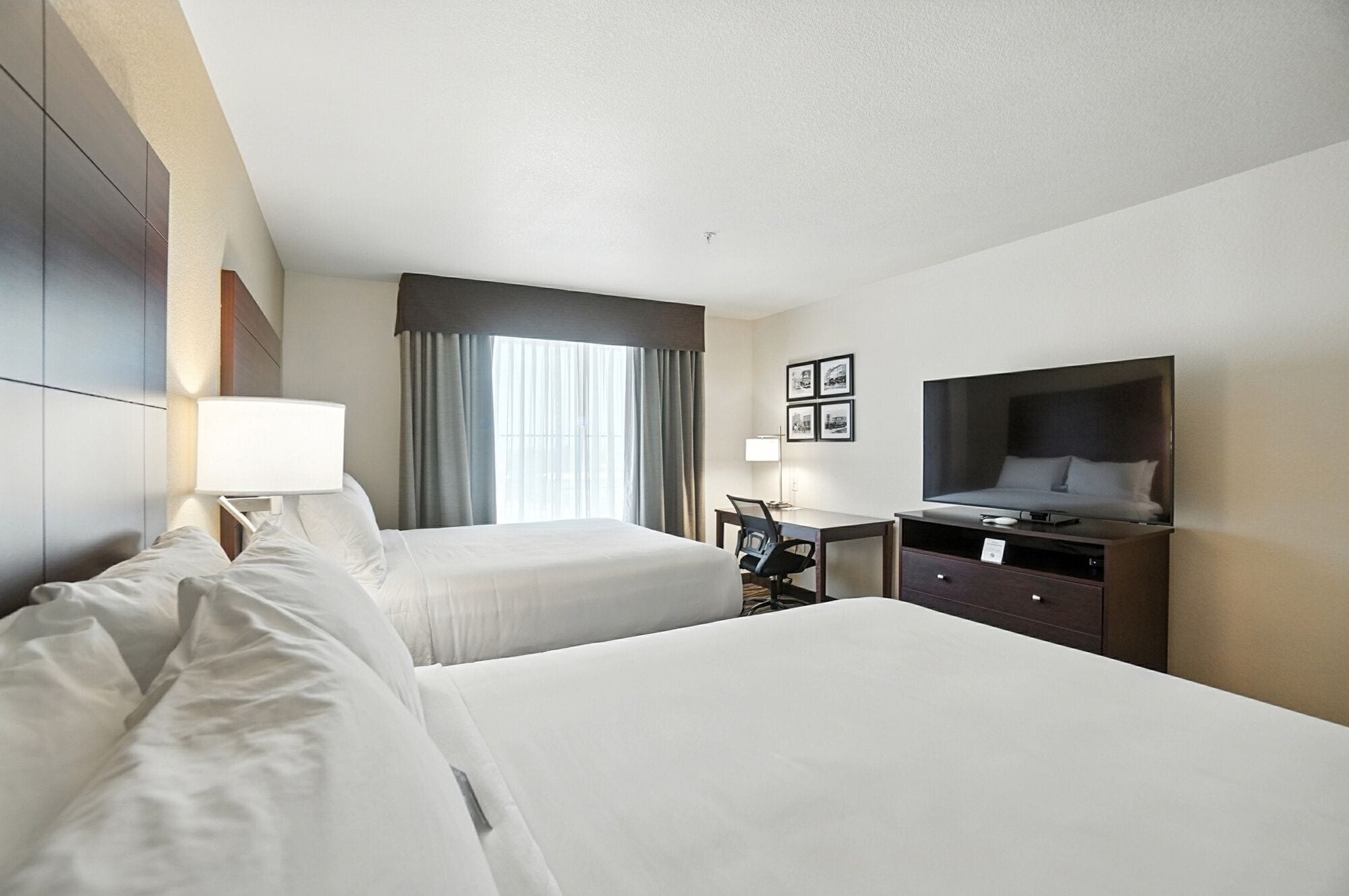 A hotel room with two beds, a desk, a chair, a TV, and a window with curtains.