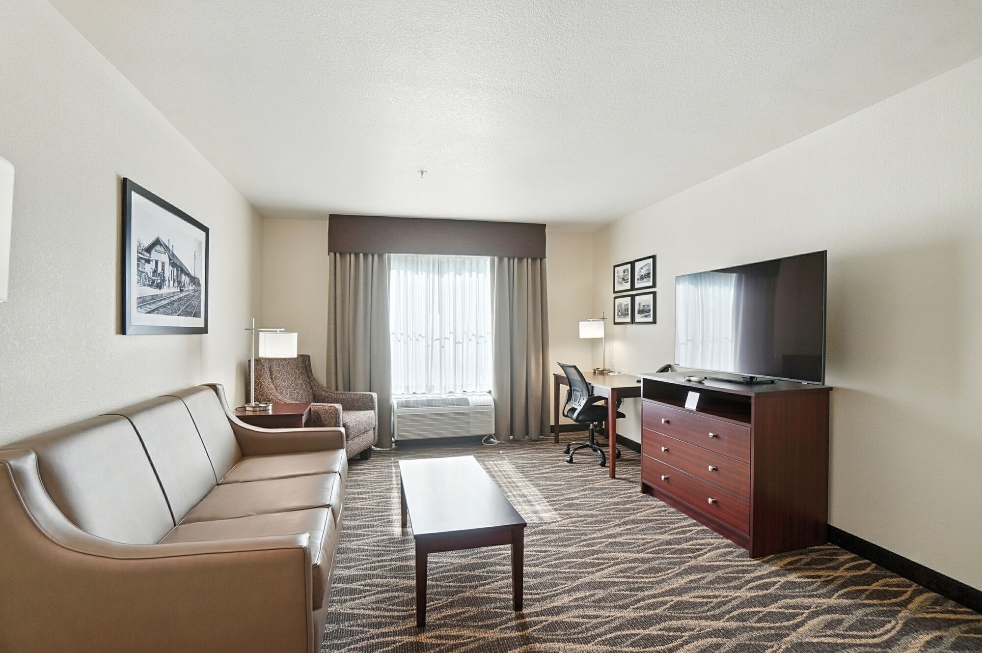 A hotel room with a sofa, a desk, a television, and a large window with curtains.