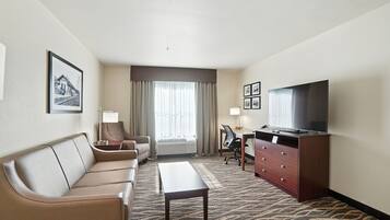 A hotel room with a sofa, a desk, a television, and a large window with curtains.