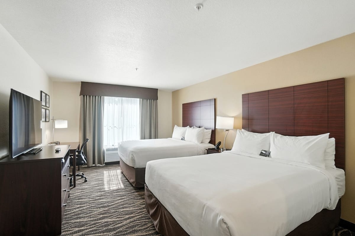 Quarto de hotel com duas camas, uma escrivaninha com computador, televisão e uma janela grande com cortinas.