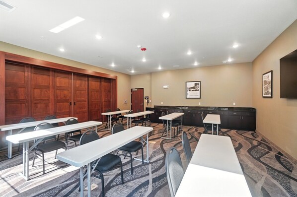 Un salón de conferencias con varias mesas y sillas, puertas de madera y piso alfombrado.