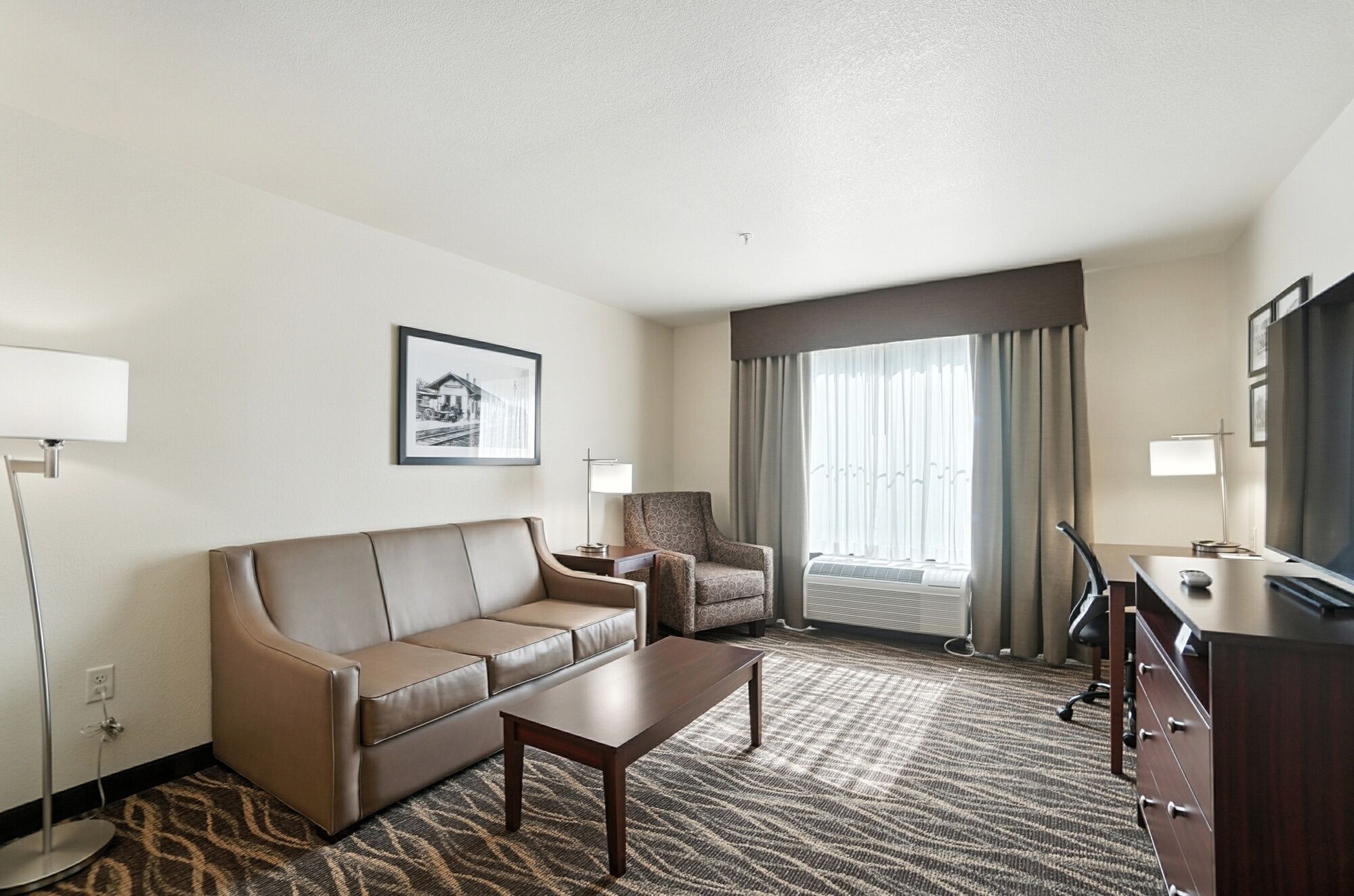 Habitación de hotel con sofá, sillón, mesa de centro y escritorio con televisor.