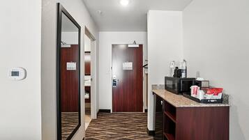 A hotel hallway with a carpeted floor, a mirror, a microwave, and a small counter with items on it.
