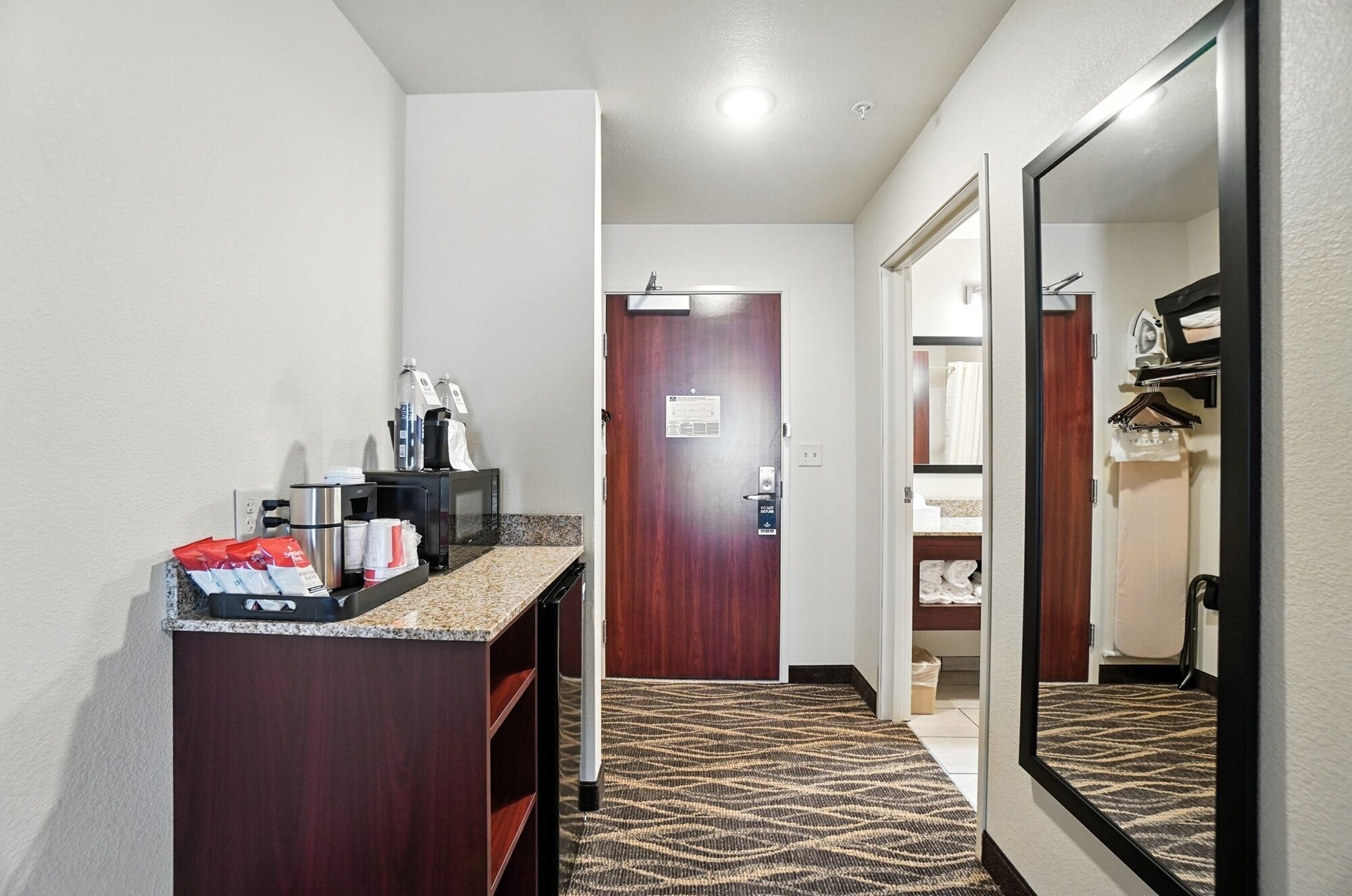 A hotel bathroom with a wooden vanity, a sink, and a mirror. There is a towel rack and a shower area visible in the background.