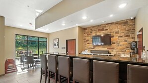 A bar area with a stone wall, a flat-screen TV, and a counter with a coffee machine. - Cobblestone Hotel & Suites-Bellefontaine (Bellefontaine)
