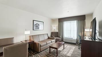 A hotel room with a sofa, a small table, a chair, a desk, a television, and a window with curtains.