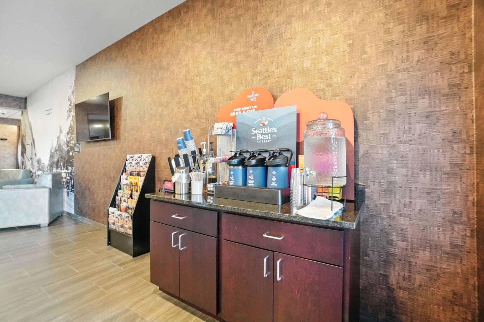 Zona de recepción con una estación de café, una vitrina de vidrio y un televisor montado en la pared.