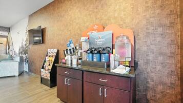 Zona de recepción con una estación de café, una vitrina de vidrio y un televisor montado en la pared.