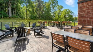 An outdoor patio with Adirondack chairs and tables, a fire pit, and a brick wall. - Cobblestone Hotel & Suites-Bellefontaine (Bellefontaine)