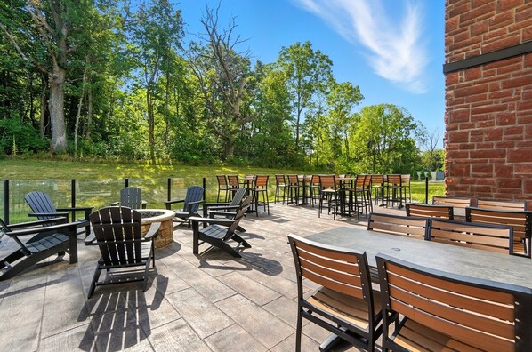 An outdoor patio with Adirondack chairs and tables, a fire pit, and a brick wall.