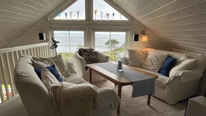 Una habitación acogedora con un sofá blanco, una mesa de madera y vista al mar a través de amplios ventanales.