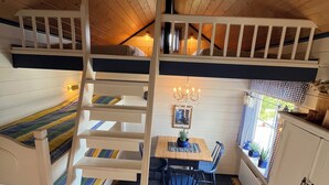 Un dormitorio acogedor en el ático con una escalera de madera, un comedor con candelabro y vistas al exterior a través de una ventana.