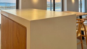 Una cocina moderna con una isla grande, iluminación colgante y amplios ventanales con vistas al mar.