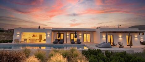 A modern house with a pool, outdoor seating, and a sunset sky.