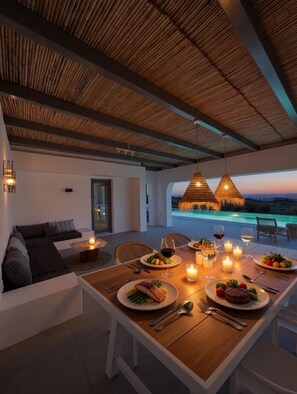 A dining area with a table set for two, candles, and a view of the ocean at dusk.