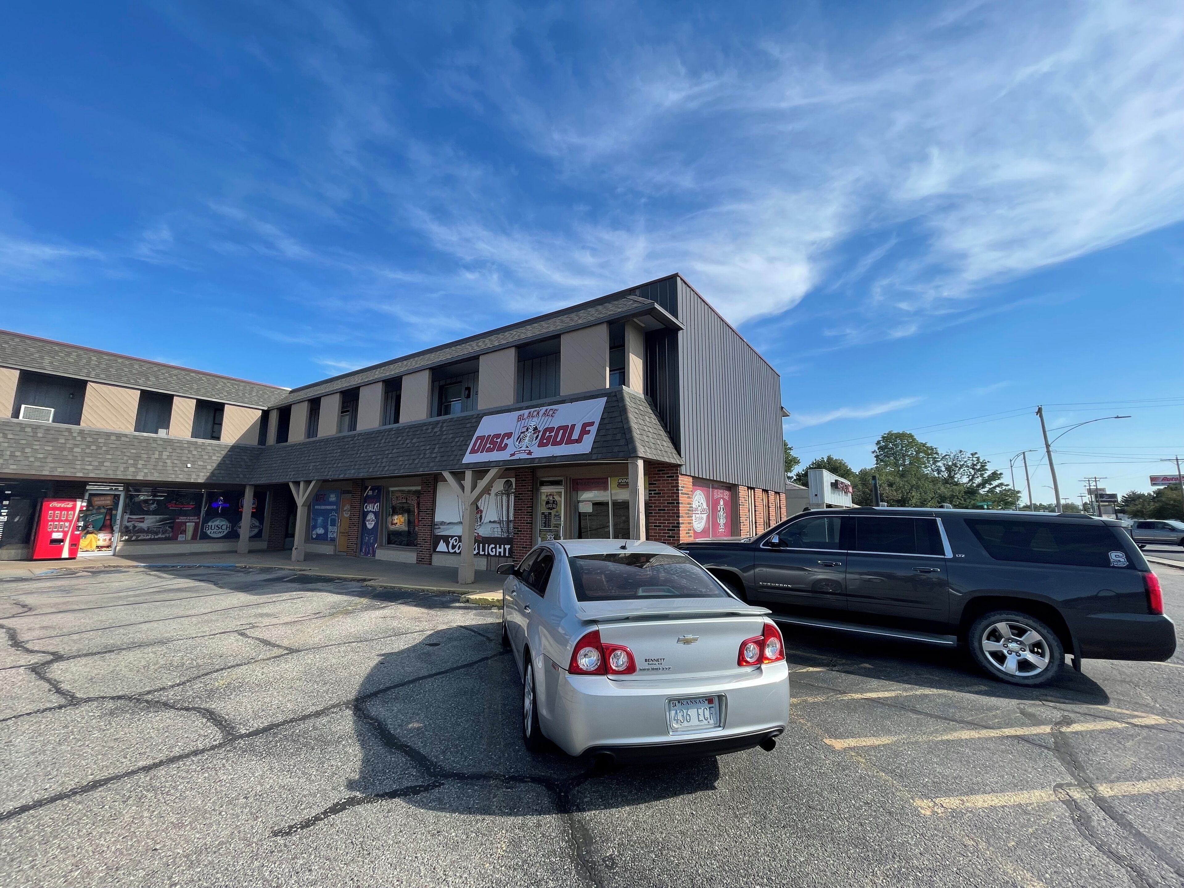 En parkeringsplads med en sølvfarvet bil og en sort SUV.