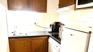 A compact kitchen with wooden cabinets, a white refrigerator, a microwave, and a sink. - Apartment for 6 people (Allos)