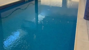 An indoor swimming pool with clear water, a lifebuoy on the wall, and a view of the outdoors through large windows. - Apartment for 6 people (Allos)
