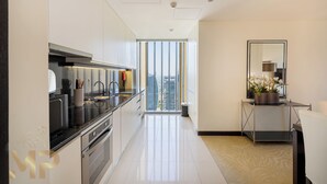 A modern kitchen with stainless steel appliances, a black countertop, and a view of the city through large windows. - Marco Polo - Chic 1BR in Marina Hub | Expansive Balcony (Dubai)