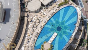 An aerial view of a hotel with a large, uniquely patterned pool, outdoor seating areas, and a circular building structure. - Marco Polo - Chic 1BR in Marina Hub | Expansive Balcony (Dubai)