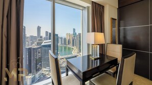 A modern hotel room with a large window offering a city view, a dining table with a lamp, and a dark-colored wall. - Marco Polo - Chic 1BR in Marina Hub | Expansive Balcony (Dubai)