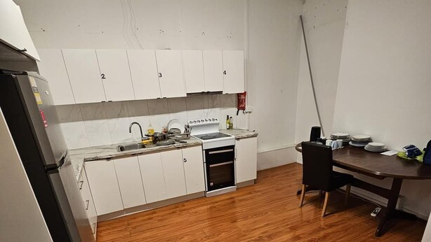 Une cuisine compacte avec des meubles blancs, un four encastré et un plancher en bois.