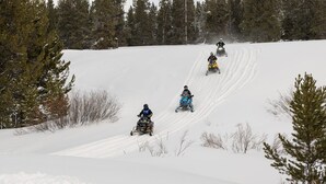 Una pendiente nevada con cuatro motos de nieve descendiendo.