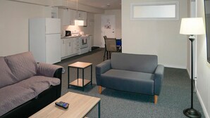 Un espacio habitable compacto con kitchenette, un sofá gris, una pequeña mesa de centro y una lámpara de pie.