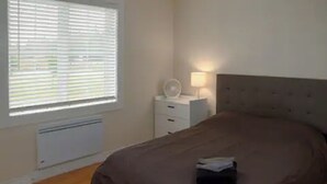 Une chambre à coucher avec un grand lit, une table de chevet avec une lampe et une fenêtre avec des stores.