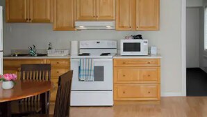 Une cuisine avec des meubles de rangement en bois, un four blanc, un four à micro-ondes et une table à manger avec des chaises.