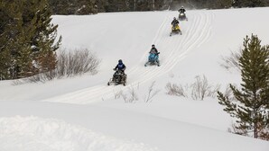 A snow-covered slope with four snowmobiles descending.