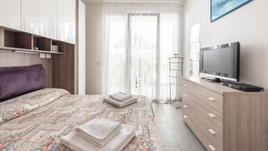 Un dormitorio moderno con cama, televisor, cómoda y ventana con cortinas translúcidas.