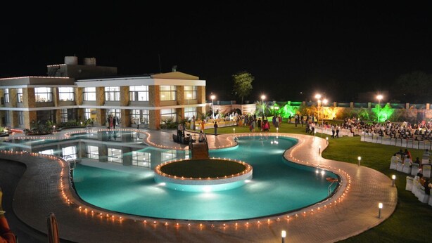 A nighttime view of a hotel with a large, illuminated swimming pool, a well-lit outdoor area, and a building with multiple windows. - Bansari Greens Resort (Aluva)