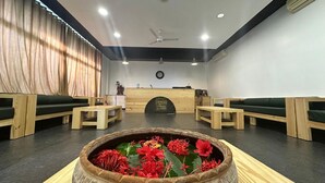 A reception area with a wooden reception desk, green cushioned seating, and a decorative flower arrangement in the foreground. - Bansari Greens Resort (Aluva)