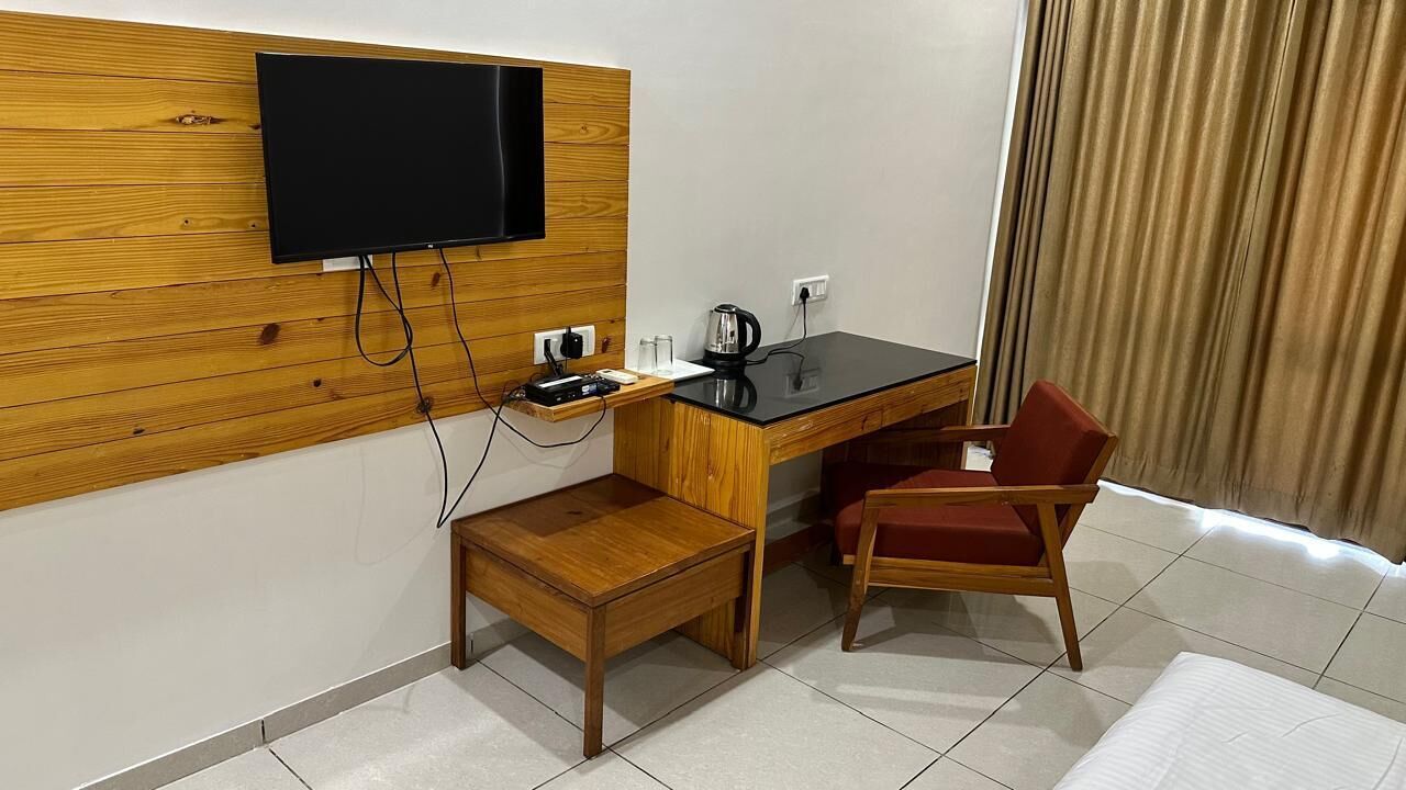Ett hotellrum med en väggpanel av trä, en platt-TV som hänger ovanför ett skrivbord, en röd stol och ett litet träbord.
